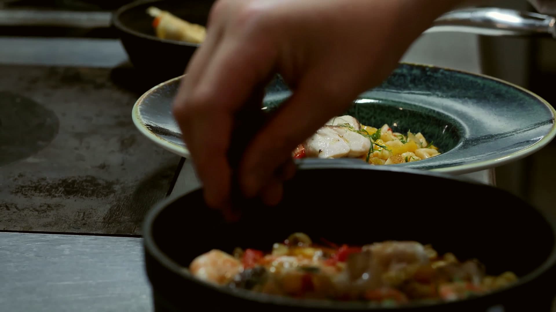 A chef’s hand finishing a dish with fresh herbs at the pass
